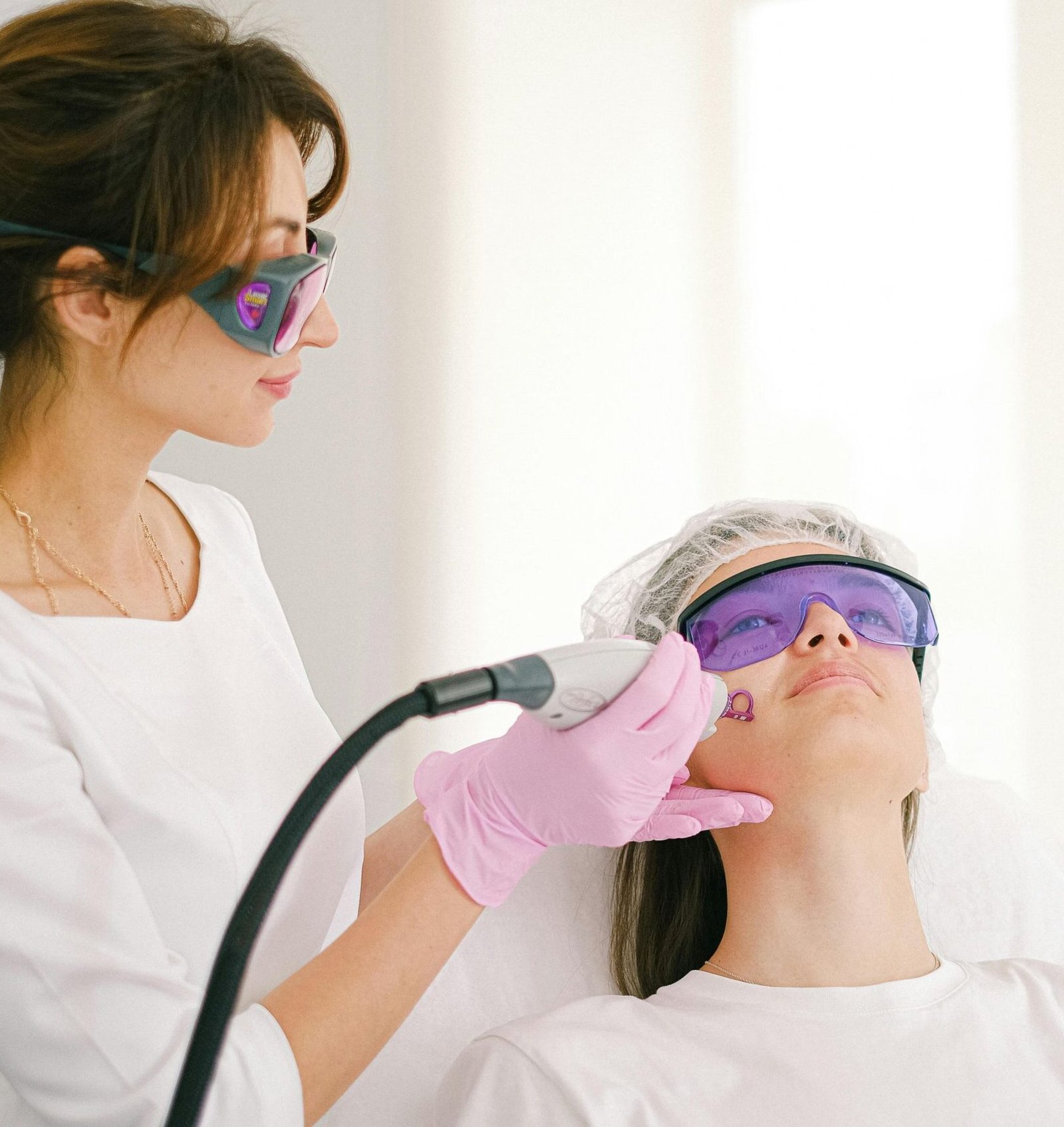 A cosmetologist performing laser treatment on a woman in a clinic setting.